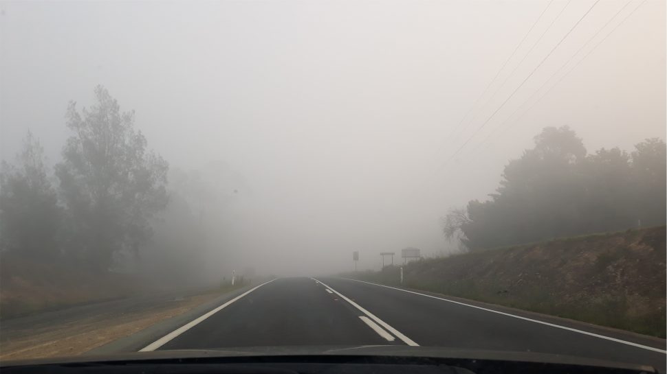 View through a car windshield of smoke obscuring the road ahead.